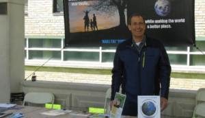 population connection staff member greeting event attendees at an outdoor event in front of a banner about making the world a better place.
