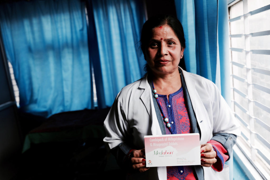 portrait of Nepalese woman with a stethascope around her neck holding a medication abortion kit