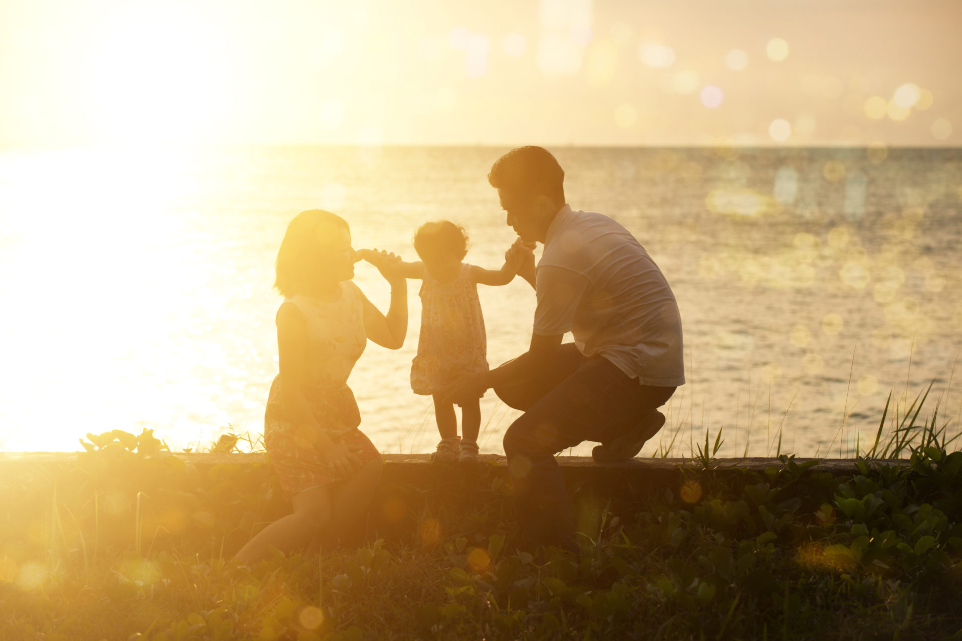 Silhouette of Asian family outdoor activity, enjoying holiday together on seaside in beautiful sunset.