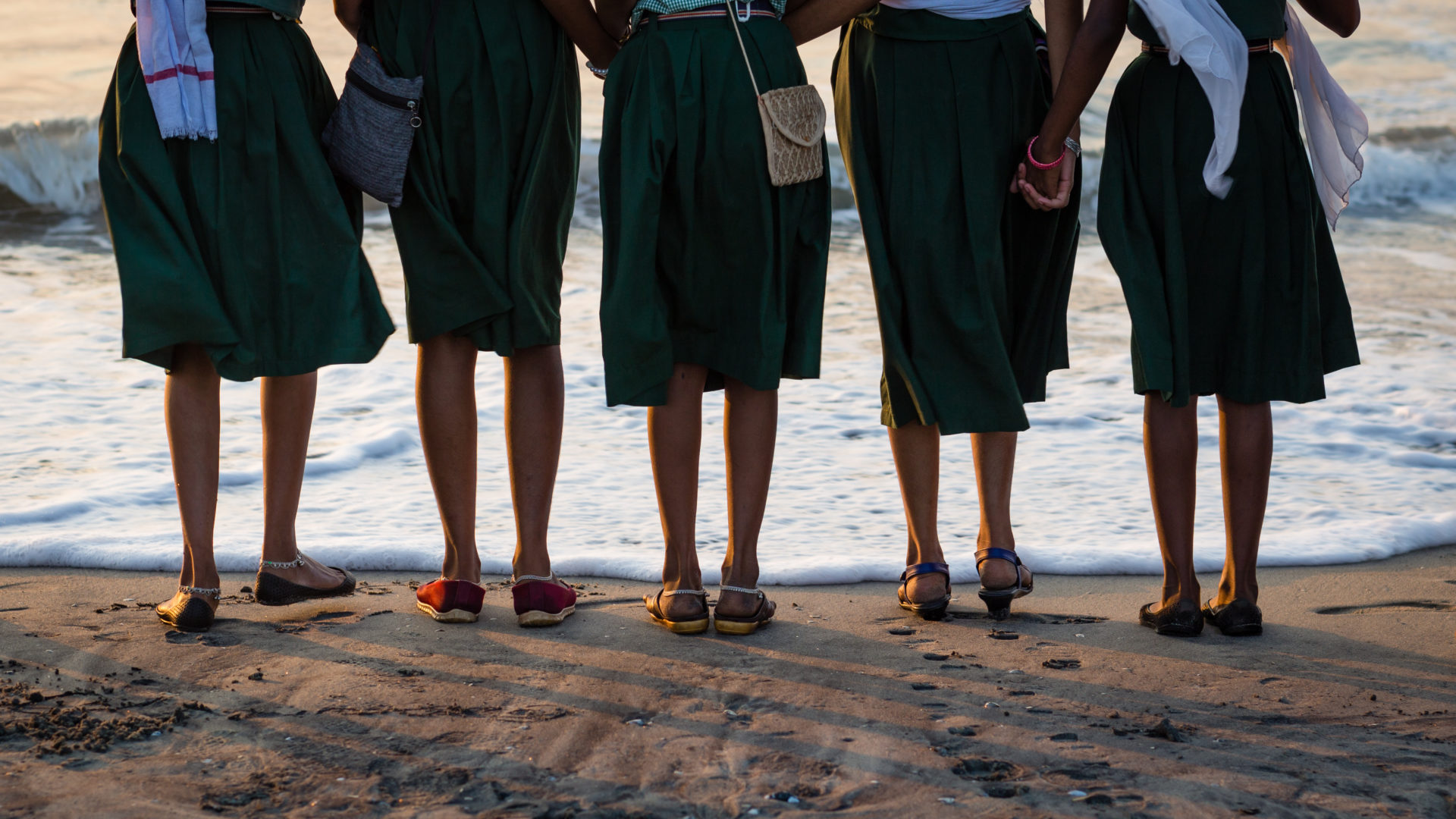 Group Of Girls Standing In Font Of The Waterline Of The Ocean At Cochin Beach, India.