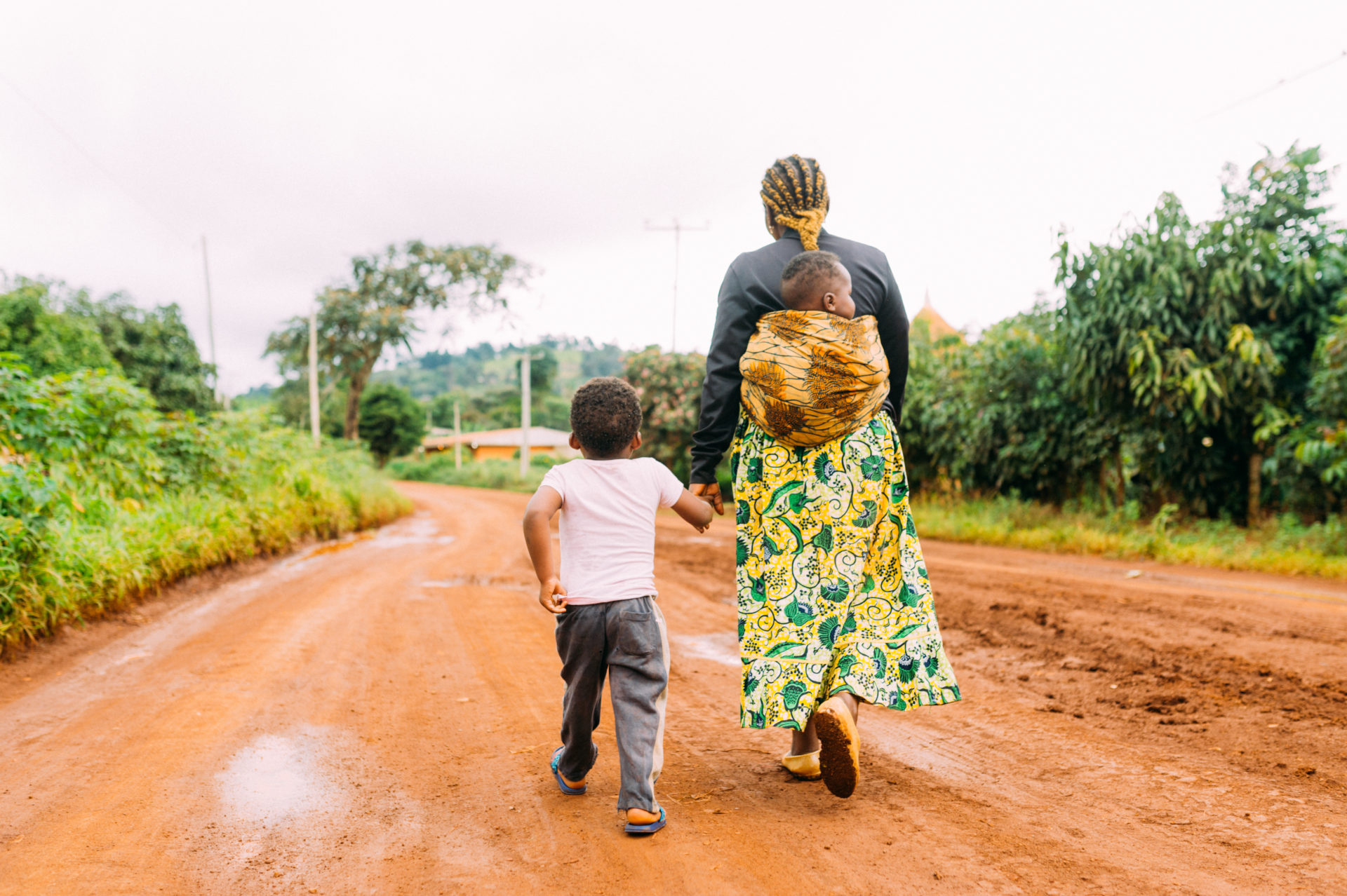 African Mother And Two Children Walk Alone In Red Clay Road In Village As A Family