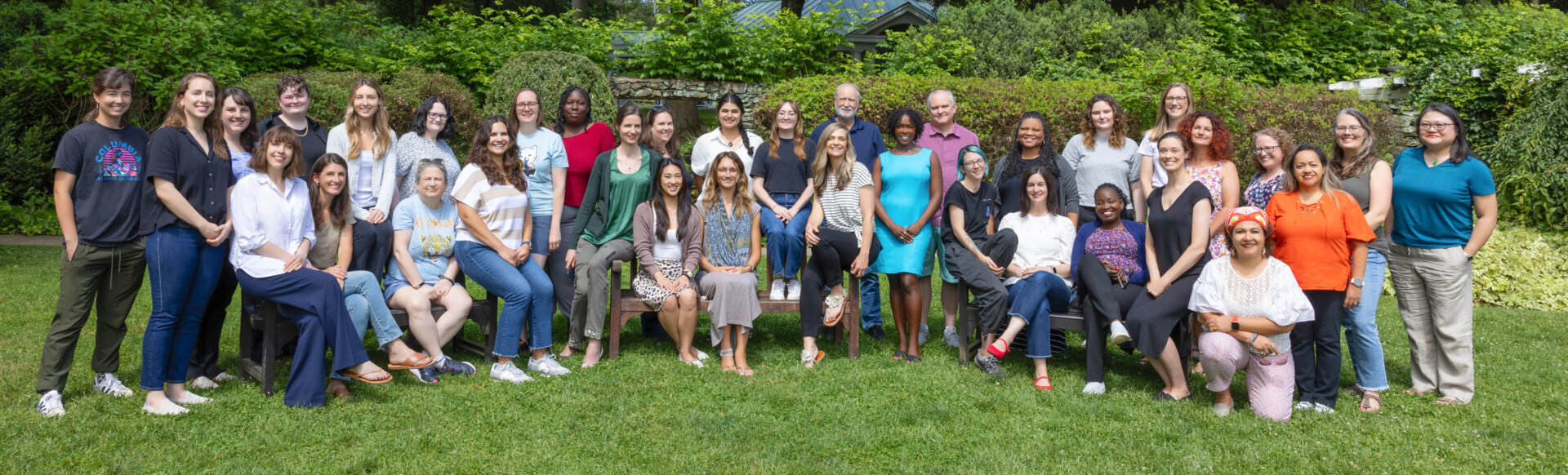 The staff of Population Connection poses together in two rows, outdoors on a lawn, in front of a backdrop of greenery.