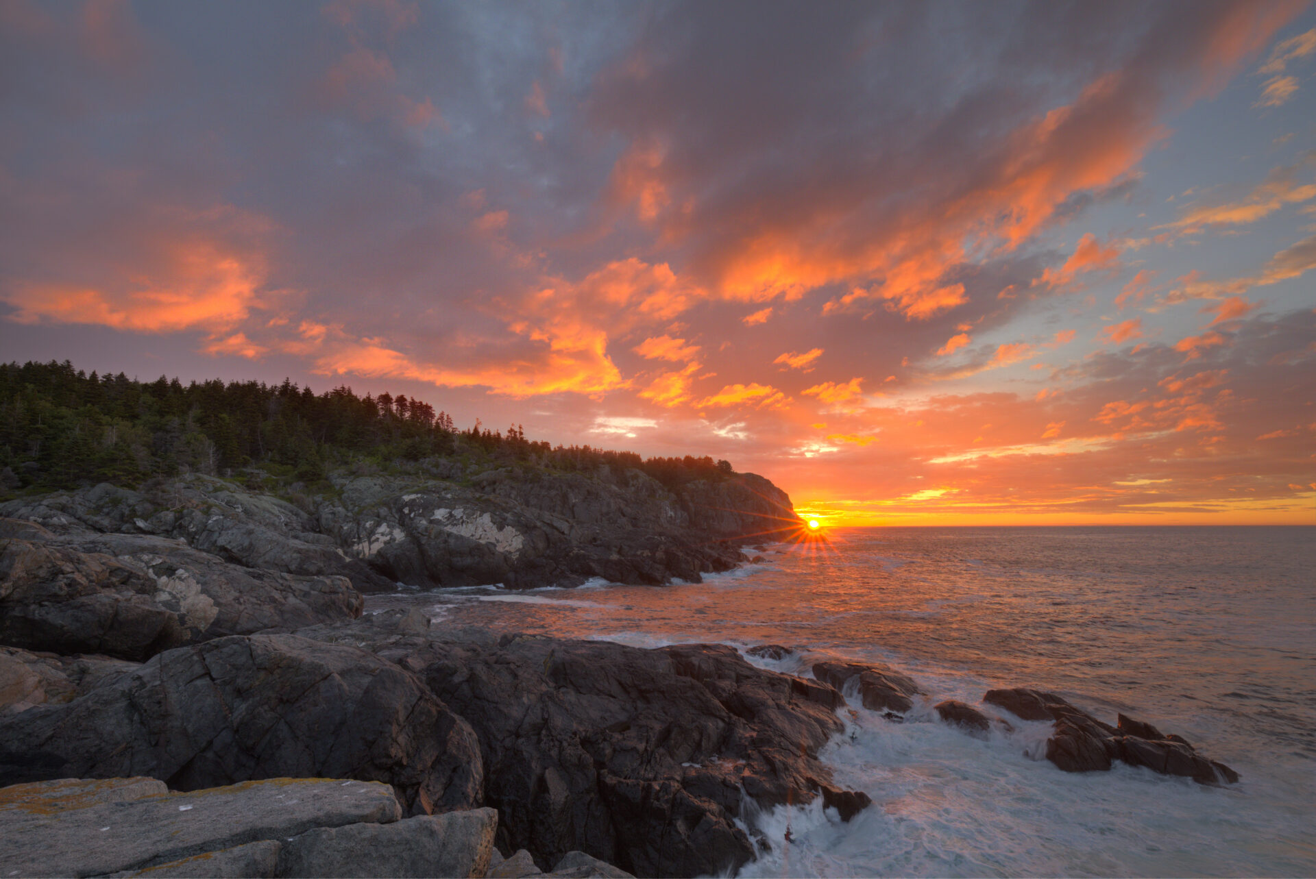 First sun peaking through Monhegan Island headlands at Black Head from Squeaker Cove. Submitted by: Tom Cameron