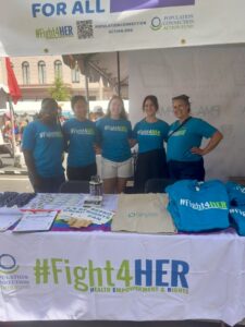 five Population Connection staff stand behind a branded #Fight4HER table covered in swag, all wearing blue #Fight4HER t-shirts