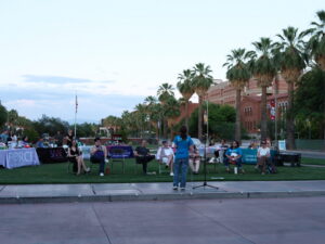 Kat speaks, with her back to the camera, to a seated audience outdoors on a university campus