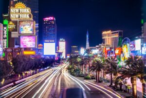 Neon-lit buildings frame a busy road in Las Vegas at night