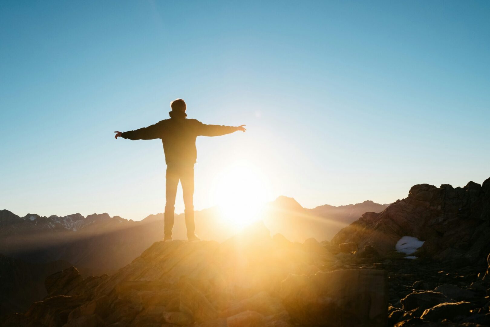 A person greets the sunrise with outstretched arms on Mt Cook in New Zealand