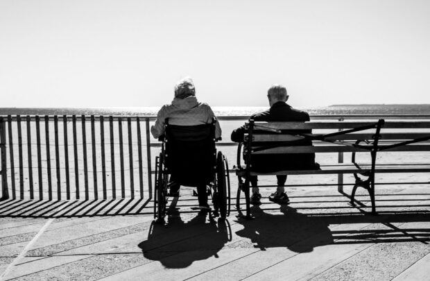 Black and white photo of two elderly people sitting on a bench facing the ocean
