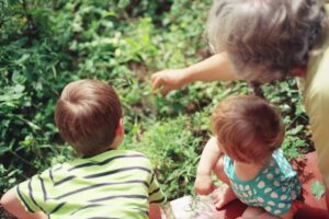 Gray haired woman playing with two young kids among plants